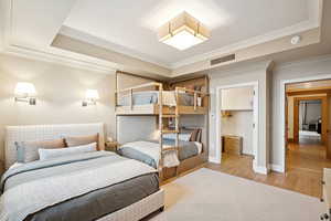 Bedroom featuring a raised ceiling, crown molding, wood finished floors, and a spacious closet