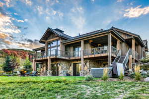 Rear view of house with a wooden deck, board and batten siding, a lawn, and stone siding