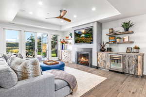 Living area featuring a raised ceiling, beverage cooler, hardwood / wood-style flooring, a large fireplace, and ceiling fan