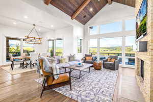 Living room featuring beamed ceiling, recessed lighting, light wood finished floors, high vaulted ceiling, and a stone fireplace