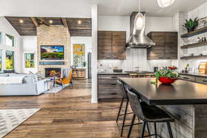 Kitchen with wall chimney exhaust hood, dark brown cabinetry, a kitchen bar, decorative backsplash, and open floor plan