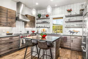 Kitchen with a kitchen island, wall chimney exhaust hood, tasteful backsplash, appliances with stainless steel finishes, and recessed lighting