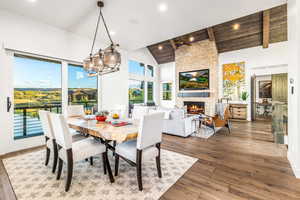 Dining space featuring a stone fireplace, beam ceiling, hardwood / wood-style flooring, a chandelier, and high vaulted ceiling