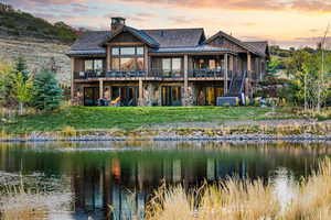 Rear view of house featuring a standing seam roof, stone siding, a water view, stairway, and a yard