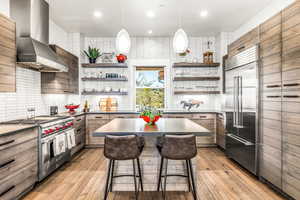 Kitchen with open shelves, high quality appliances, a kitchen island, wall chimney range hood, and a breakfast bar