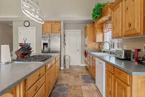 Kitchen with stone tile floors, appliances with stainless steel finishes, dark countertops, and decorative light fixtures
