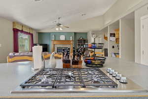 Kitchen with a glass covered fireplace, stainless steel gas cooktop, vaulted ceiling, light countertops, and ceiling fan