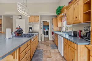 Kitchen featuring open shelves, dark countertops, stone tile flooring, stainless steel appliances, and hanging light fixtures