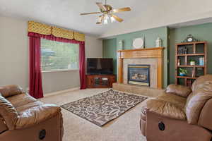 Living area featuring a fireplace, carpet flooring, a textured ceiling, a ceiling fan, and vaulted ceiling