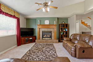 Living area featuring lofted ceiling, light carpet, a tiled fireplace, a ceiling fan, and stairway
