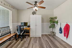 Office space with a decorative wall, wainscoting, wood finished floors, and ceiling fan