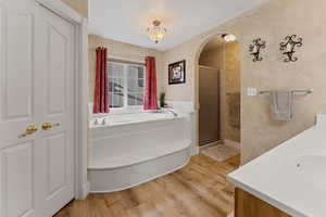 Bathroom with double vanity, a garden tub, a shower stall, and light wood-style floors