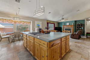 Kitchen with a kitchen island, a fireplace, hanging light fixtures, stone tile flooring, and vaulted ceiling