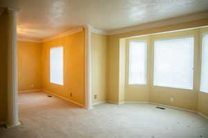 Empty room with ornate columns, a textured ceiling, carpet floors, and crown molding