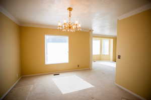 Empty room featuring ornamental molding, a chandelier, carpet flooring, and a textured ceiling