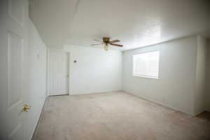 Empty room featuring light carpet, a ceiling fan, and a textured ceiling