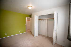 Unfurnished bedroom with a textured ceiling, light carpet, and a closet