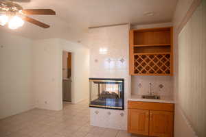 Indoor wet bar with light countertops, brown cabinetry, light tile patterned floors, open shelves, and decorative backsplash