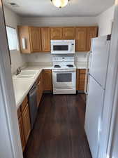 Kitchen with white appliances, light countertops, dark wood finished floors, brown cabinets, and a textured ceiling