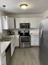 Kitchen with appliances with stainless steel finishes, light countertops, white cabinets, and a textured ceiling