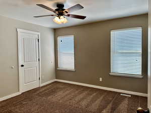Master bedroom with dark carpet, ceiling fan, double windows with a large closet and bath