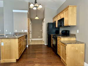 Kitchen with dark stone countertops, black appliances, pendant lighting, dark wood-style floors, and light brown cabinets