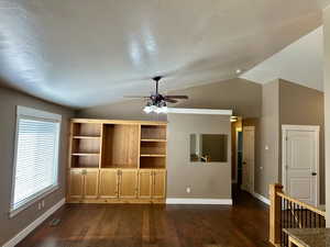 This great room with vaulted ceiling, dark wood-type flooring, a ceiling fan, and a textured ceiling features beautiful built-in shelving