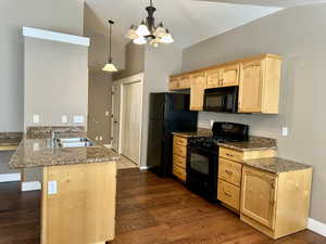 Kitchen featuring black appliances, light brown cabinets, a peninsula, pendant lighting, and lofted ceiling