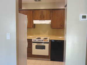 Kitchen featuring white appliances, light countertops, under cabinet range hood, and brown cabinetry