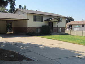 Bi-level home featuring brick siding, concrete driveway, roof with shingles, and an attached carport