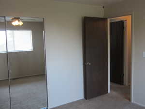 Unfurnished bedroom featuring light colored carpet, a closet, and a ceiling fan