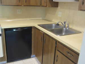 Kitchen with black dishwasher, light countertops, and brown cabinets