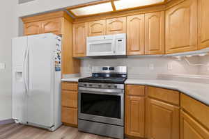 Kitchen with white appliances, light countertops, light wood-style floors, and light brown cabinetry