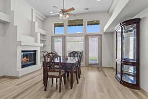 Dining room featuring light wood-style floors, a glass covered fireplace, built in features, a ceiling fan, and recessed lighting