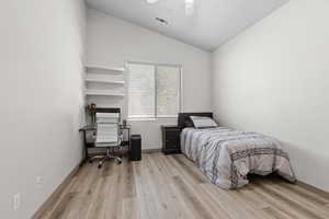 Bedroom with vaulted ceiling, light wood-style floors, a desk, a textured ceiling, and a ceiling fan