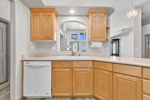Kitchen with light brown cabinets, white dishwasher, light countertops, hanging light fixtures, and light wood-type flooring