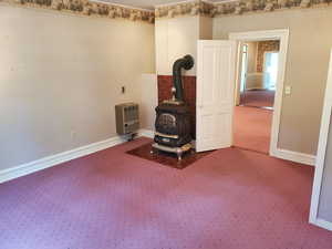 Unfurnished room with a wood stove, carpet, and heating unit