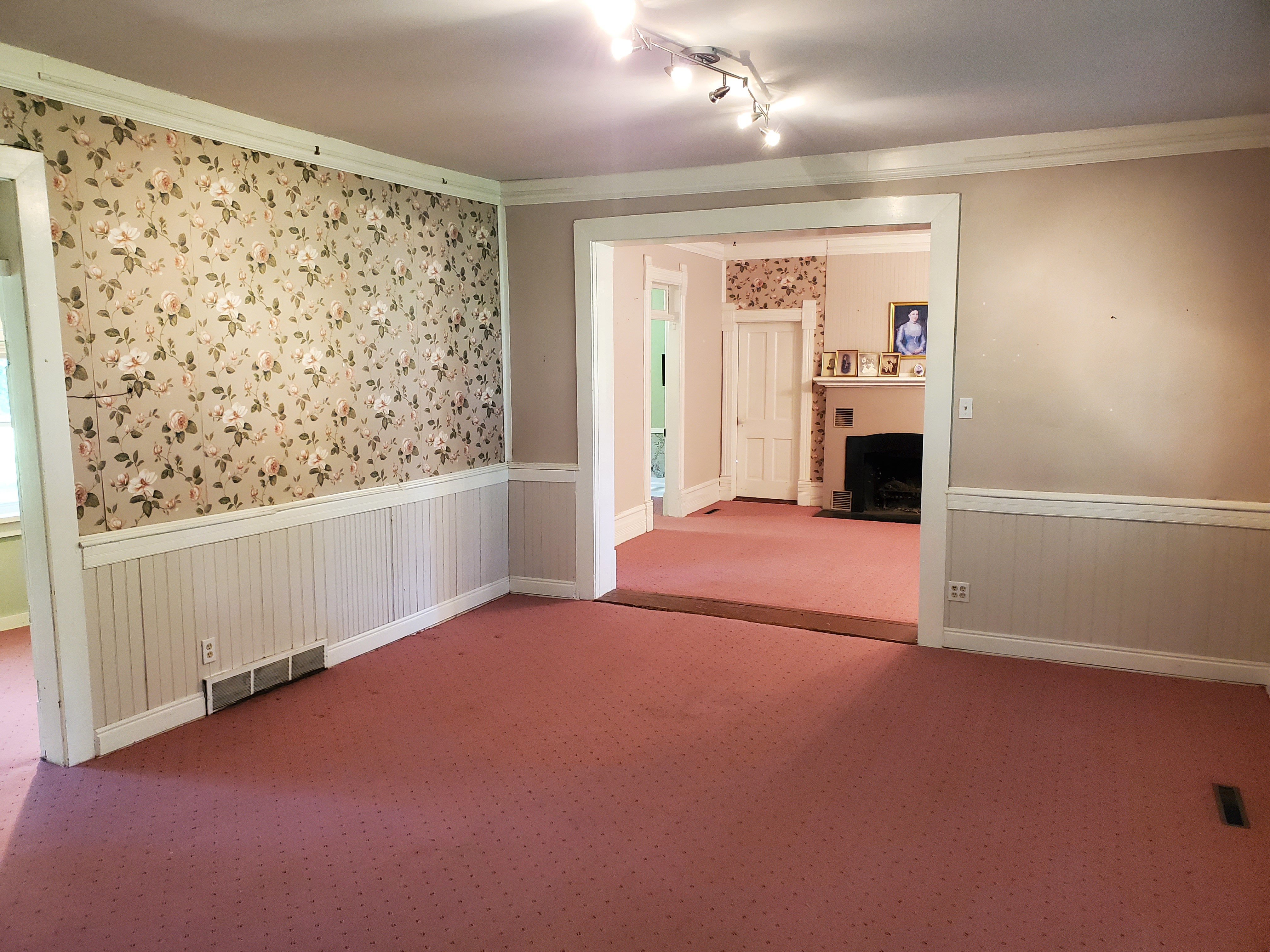 Carpeted spare room featuring wallpapered walls, crown molding, a wainscoted wall, a fireplace with flush hearth, and rail lighting