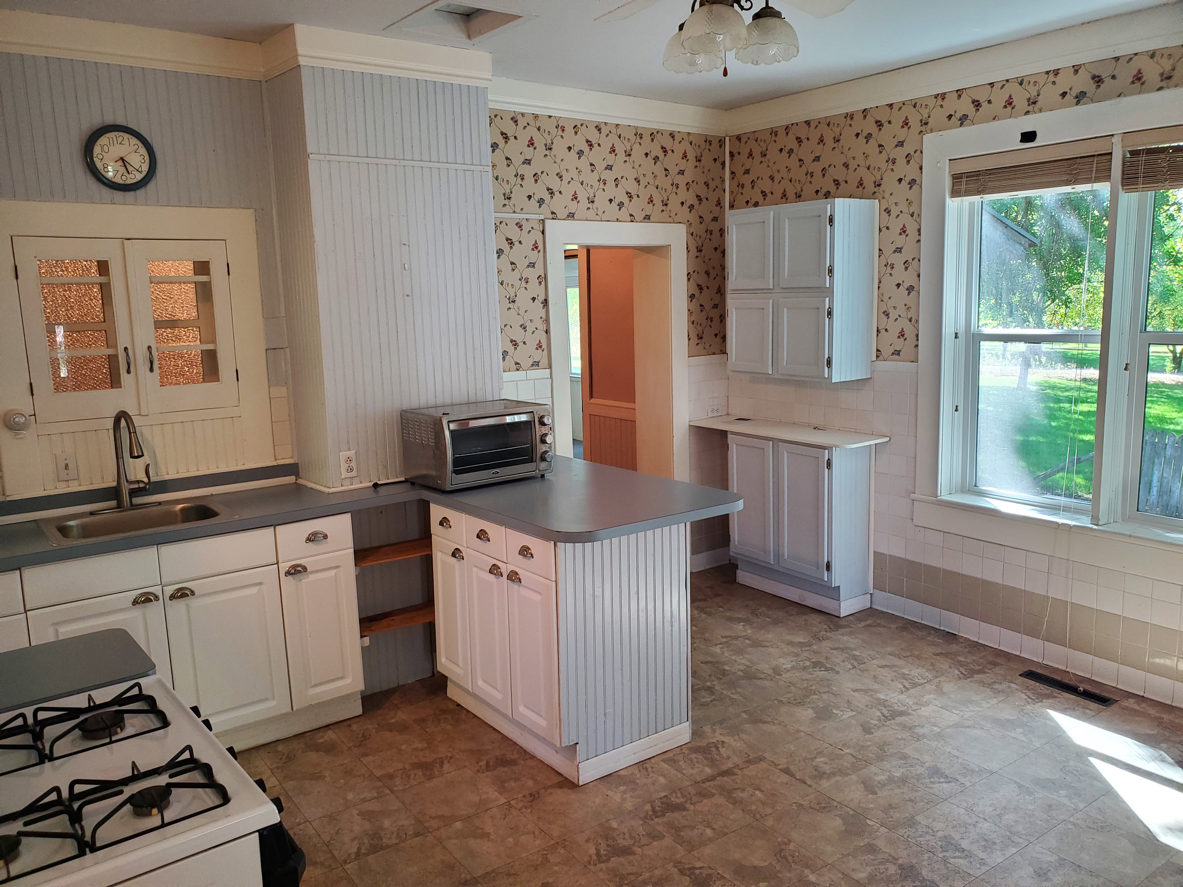Kitchen featuring white cabinetry, white gas stove, wainscoting, wallpapered walls, and ceiling fan