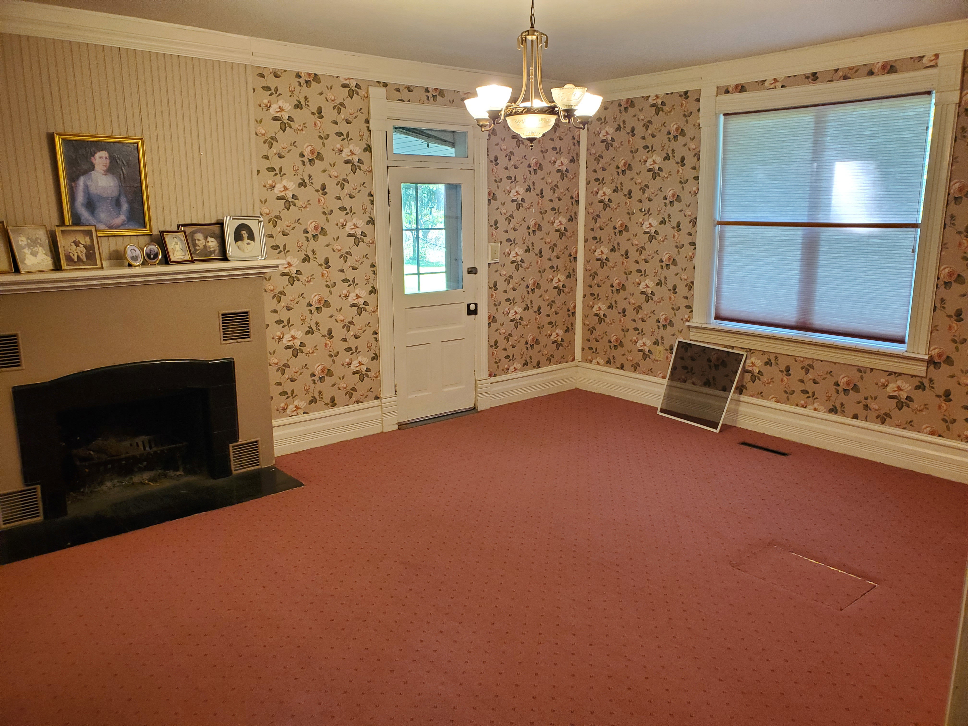 Unfurnished living room featuring wallpapered walls, ornamental molding, a chandelier, a fireplace with flush hearth, and carpet floors