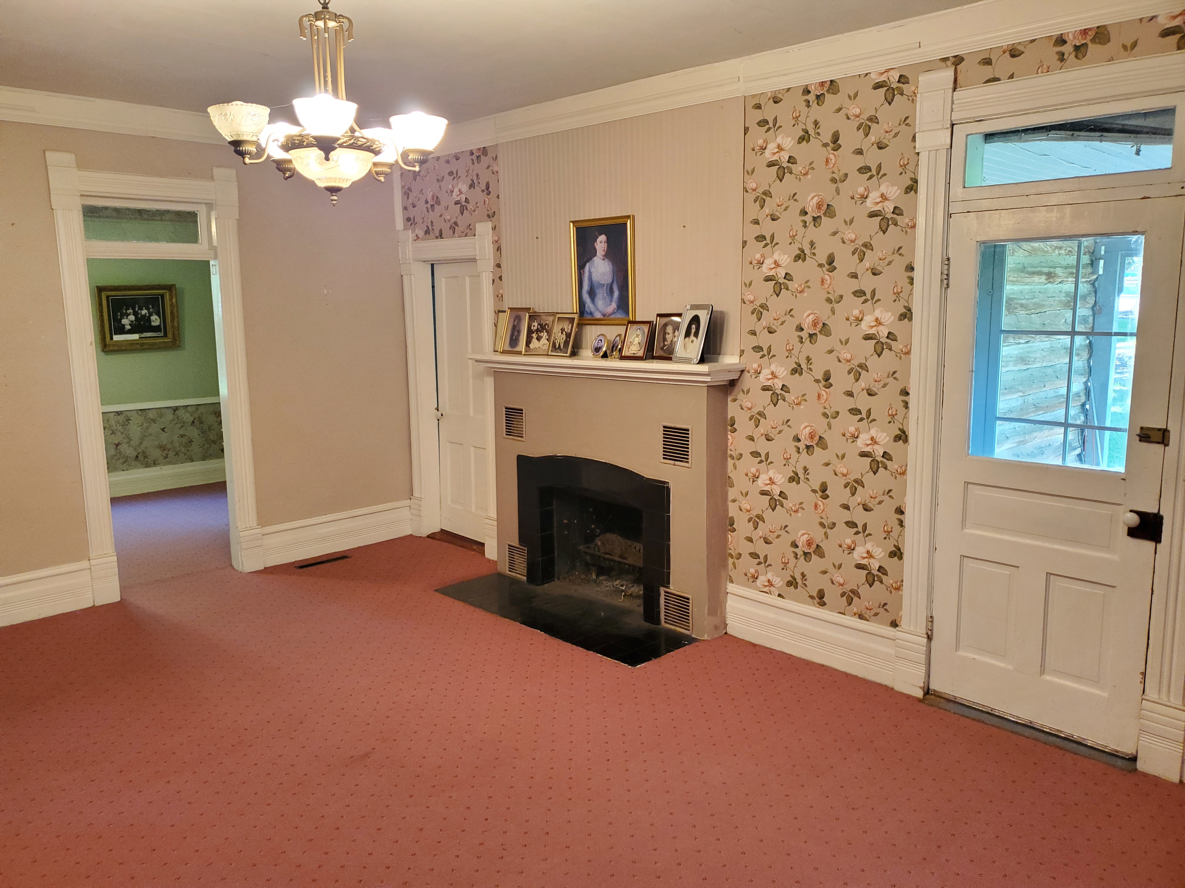 Unfurnished living room with wallpapered walls, crown molding, a fireplace with flush hearth, carpet flooring, and a chandelier