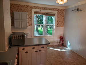 Kitchen featuring a peninsula, wallpapered walls, a wainscoted wall, dark countertops, and tile walls