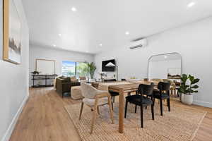 Dining area with light wood-style floors, an AC wall unit, and recessed lighting