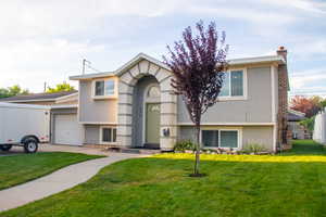 View of front of home with stucco siding, a chimney, a front yard, a garage, and driveway