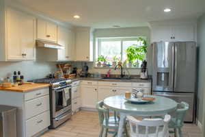 Kitchen featuring stainless steel appliances, white cabinetry, under cabinet range hood, wood tiled floors, and recessed lighting