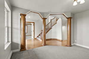 Spare room featuring decorative columns, carpet, baseboard heating, stairway, and wood finished floors