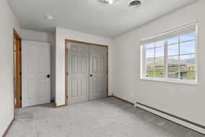 Unfurnished bedroom with baseboard heating, a mountain view, light colored carpet, and a closet