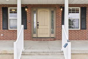 Property entrance featuring covered porch and brick siding