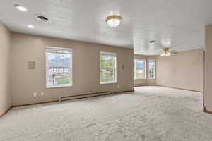 Empty room with carpet, healthy amount of natural light, a baseboard heating unit, and a textured ceiling