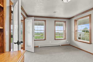 Carpeted entryway with crown molding, a baseboard heating unit, plenty of natural light, and a textured ceiling